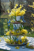 Self-made cake stand made of plates and milk pots, decorated with gold bells and grape hyacinths, Easter eggs in a wreath