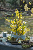 Spring decoration with gold bells and daffodils bouquets in bottles, tied with ribbon on a bowl with moss