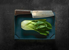 Bok choy in a wooden crate with a meat cleaver