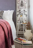 Bed, white bedside table and lamp against patterned wallpaper