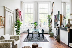 Glass table with chairs in front of lattice windows, faux fireplace and houseplants in period building