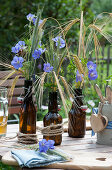 Table decoration with cranesbill and ears of cereal in beer bottles, cutlery in beer mug with wooden heart as decoration