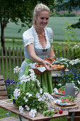 Woman sets the table for the Bavarian snack: plate with radishes and pretzels on wooden discs, beer mug