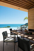 Dining table on roofed terrace with swimming pool and sea view