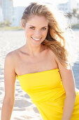 A blonde woman on a beach wearing a yellow bandeau dress