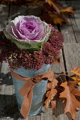 Ornamental cabbage and sedums in metal vase with brown ribbon