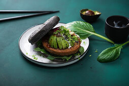 Soy wheat protein patty with avocado, radishes and two sauces in a black burger bun