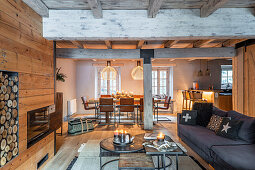 Sofa set in front of fireplace, wood-panelled walls and dining area and kitchen in background