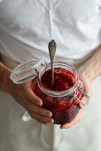 The man holds a jar of homemade strawberry jam in his hands