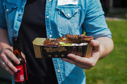 A person holding a cardboard tray of grilled spare ribs