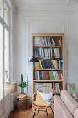 Bookcase, rattan chair and standard lamp next to window in living room