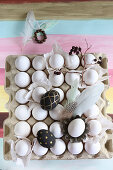 Painted eggs, feathers and twig on crate of white eggs