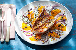 Fried fish fillets on an orange and onion salad with fennel and edible flower petals