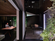 Woman sitting at dining table with view of courtyard garden at night