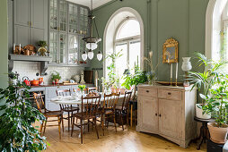 Dining table, houseplants, green walls and arched windows in kitchen with high ceiling