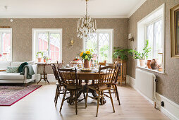 Crystal chandelier in dining area of bright, open-plan interior with patterned wallpaper