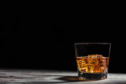 Glass of scotch in rays on aged rustic table in darkness