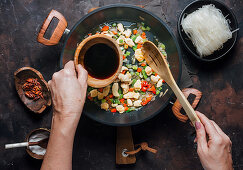 Pouring soy sauce into pan with chopped chicken and vegetables while preparing delicious noodles
