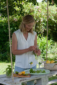 Woman opens bottle with syrup, glasses with mint and orange slice, hanging pallet as a table