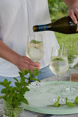 Woman fills glasses with Prosecco, fresh mint bouquet