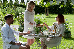 Friends at the set table in the garden, woman hands bread