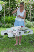 White pallet as a seat hung from a tree with ropes, woman pours a drink