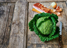 Savoy cabbage, bacon and onions on a wooden background
