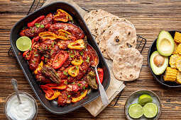 Wurstauflauf mit Mini-Paprika serviert mit Tortillas, Avocado und Mais