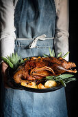 Woman serving roasted duck with fried apples and sage