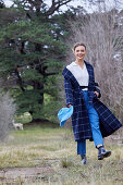 A blonde woman in a garden wearing a long, checked coat