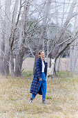 A blonde woman in a garden wearing a long checked coat