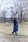 A blonde woman in a garden wearing a long, checked coat