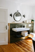 Sink with two sets of taps against green wall tiles with wooden frame