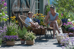 Mother and son sit on an insect-friendly terrace with blooming basil, Echinacea, mallow, fan flower 'Violet Blue', bidens 'Bee White', rosemary