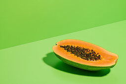 Fresh ripe halved papaya with seeds placed on bright green background