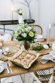 A tray on buns and a bouquet of flowers on a table laid for an Easter meal