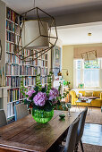 A wooden table with a bouquet of flowers in front of a floor-to-ceiling bookshelf