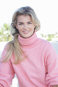 A young blonde woman wearing a pink turtle-neck jumper