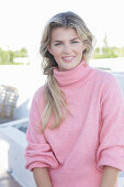 A young blonde woman wearing a pink turtle-neck jumper