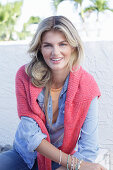 A young blonde woman wearing a denim shirt with a coral-coloured jumper over her shoulders