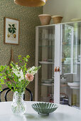 View past flowers on table to glass-fronted cabinet