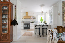 An antique crockery cupboard in a passageway with a breakfast bar in a white kitchen