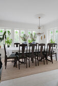 A long dining table with upholstered wooden chairs in front of the window