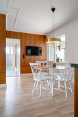 A dining area with a round, white table and chairs and a brass lamp pendant lamp