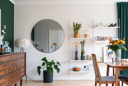 Sideboard vor grüner Wand, runder Spiegel und offenes Regal im Esszimmer