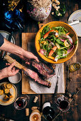 Carved tomahawk steak on a table laid with a mixed leaf salad and sweetcorn