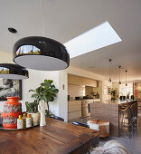 Black ceiling lamps above dining table in front of open-plan kitchen
