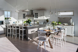 Open plan kitchen and dining room with sea views Bar stools at island unit with dining table and chairs in sunlit coastal home