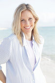 A blonde woman by the sea wearing a blue-and-white striped shirt