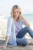 Blonde Frau in blau-weiß gestreiftem Hemd und Jeans am Meer